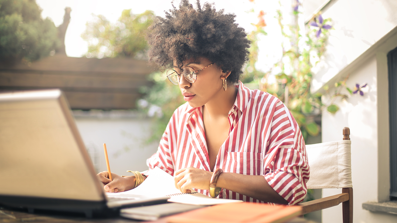 A young woman working on her laptop at a table outside.