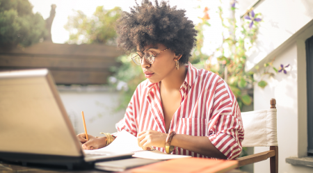 A young woman working on her laptop at a table outside.